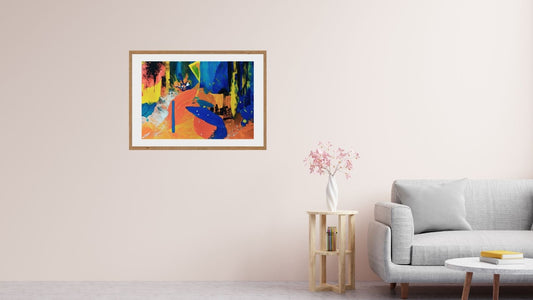 An abstract multicolored artwork in a frame hanging on a wall over a sofa, with a wooden side table and a plant beside it.